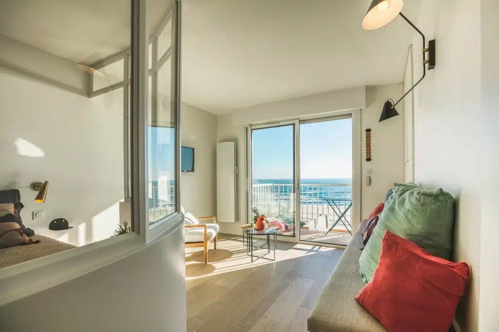 Vue d'une rénovation intérieure d'un appartement en bord de mer avec un design moderne et lumineux, intégrant une ouverture sur un balcon offrant une vue panoramique sur l'océan.